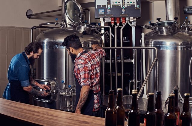 Two bearded hipster males in an apron working in a brewery factory. Two bearded hipster males in an apron working in the brewery factory.